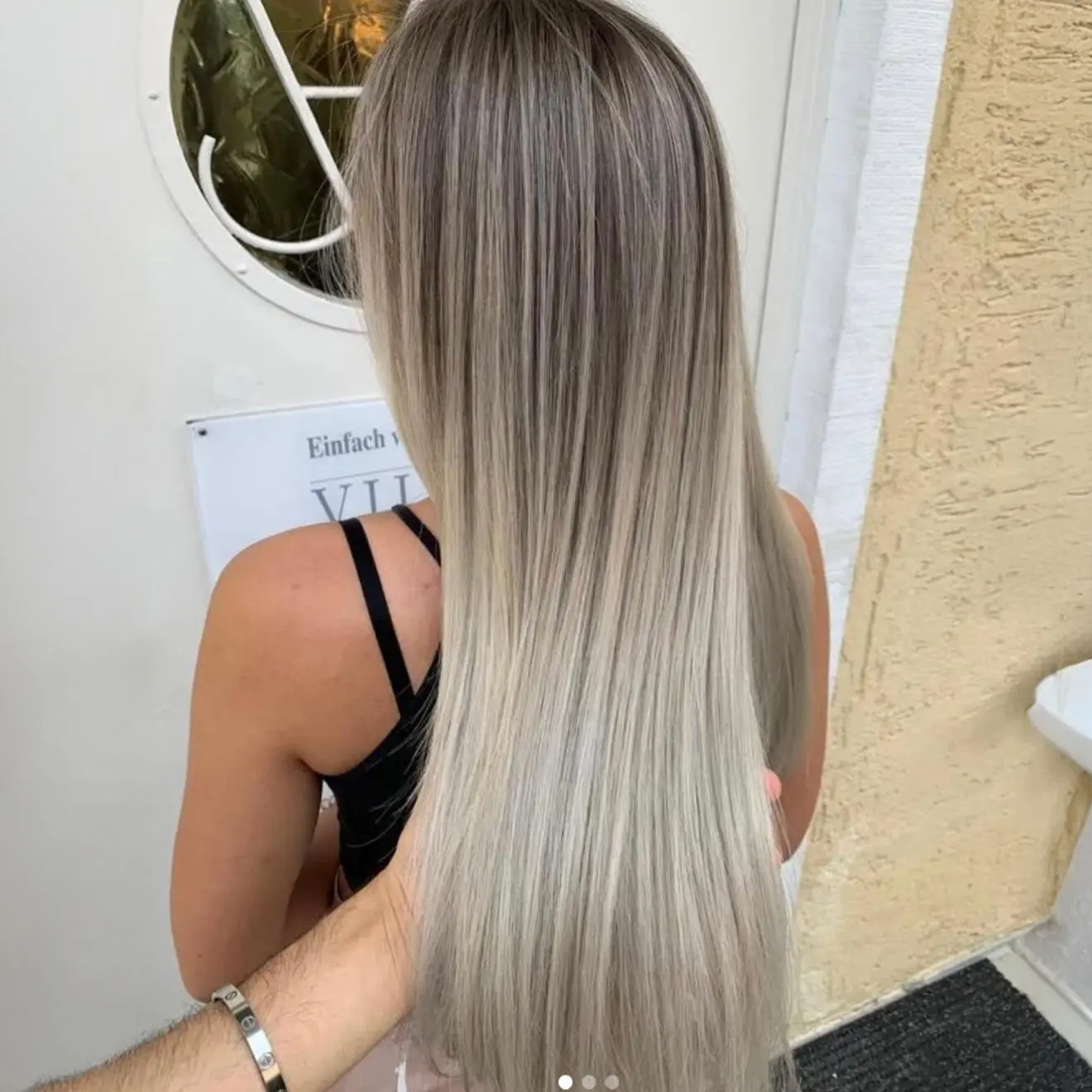 insta5 Person mit langem, glattem, aschblondem Haar in der Nähe einer weißen Tür.